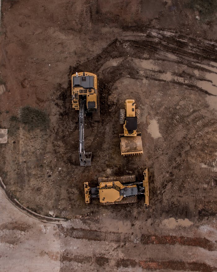 About An aerial shot of heavy machinery at a construction site, including excavators and road rollers.